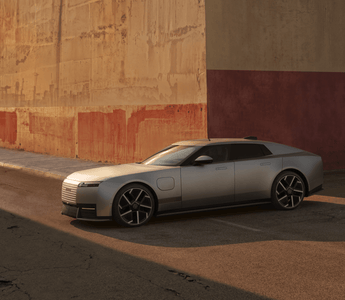 Silver Jaguar Type 01 electric grand tourer parked beside a weathered industrial wall in warm evening light.