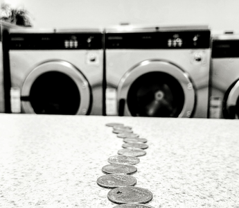 Row of washing machines with coins lined up on a counter, symbolising the concept of money laundering.