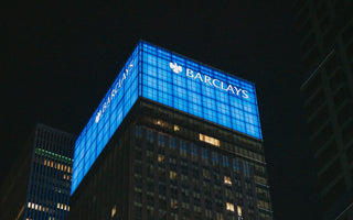 Barclays office tower at night, with its name and eagle logo illuminated against blue panels above the windows.