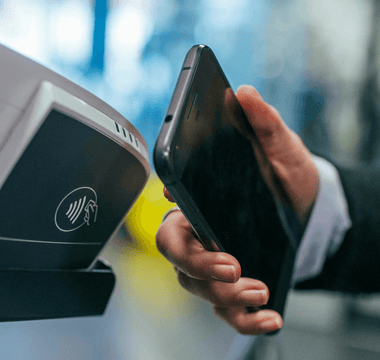 Hand holding a smartphone over a contactless payment terminal, illustrating the shift from cash to digital payments.