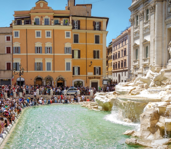 Crowds of tourists gathered around Rome’s Trevi Fountain on a sunny day, with visitors lining the edge of the fountain’s turquoise water and historic buildings in the background.
