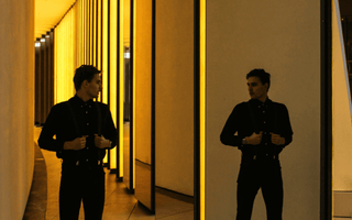 Man standing between mirrored golden walls, representing the challenge of balancing two full-time jobs and identity conflict.