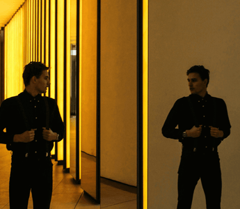 Man standing between mirrored golden walls, representing the challenge of balancing two full-time jobs and identity conflict.
