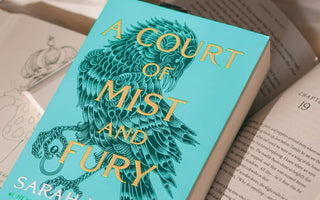 Close-up of the novel A Court of Mist and Fury by Sarah J Maas resting on an open book, representing the bestselling romantasy series published by Bloomsbury.