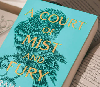 Close-up of the novel A Court of Mist and Fury by Sarah J Maas resting on an open book, representing the bestselling romantasy series published by Bloomsbury.