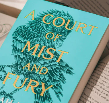 Close-up of the novel A Court of Mist and Fury by Sarah J Maas resting on an open book, representing the bestselling romantasy series published by Bloomsbury.