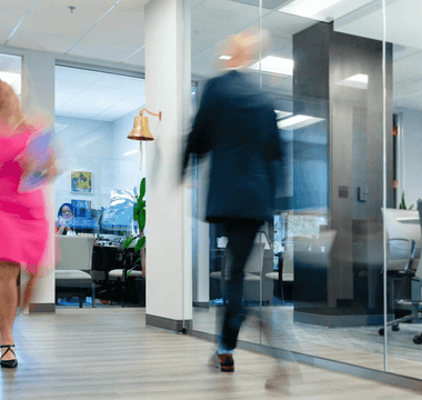 Two blurred professionals walking quickly through a modern office corridor, illustrating busyness and constant activity at work.