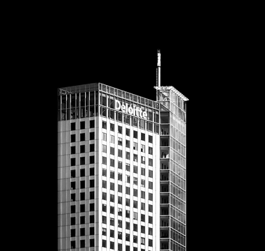 Deloitte office tower against a black background, symbolising corporate success and executive pay at Deloitte UK.