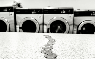 Row of washing machines with coins lined up on a counter, symbolising the concept of money laundering.