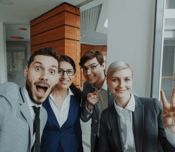 A group of cheerful young professionals taking a selfie together in a modern office — symbolising workplace friendships, collaboration, and the human connection explored in KPMG’s Friends at Work 2.0 report.