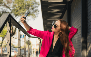 Young woman in a pink jacket taking a selfie outdoors, illustrating social media-driven shopping and fashion returns culture.