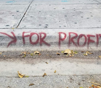 Graffiti on a pavement reading “For Profit” with an arrow, symbolising the focus on profit over long-term business strength.