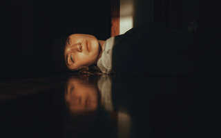Woman resting on the floor in a dimly lit office, representing workplace wellbeing and the growing acceptance of rest at work.