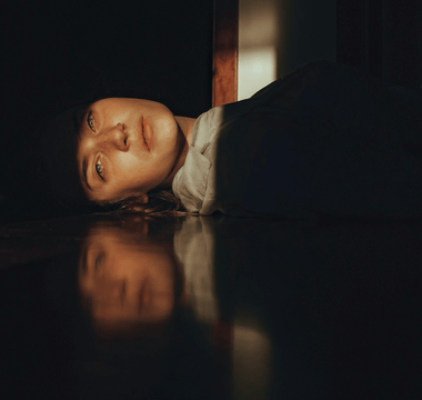 Woman resting on the floor in a dimly lit office, representing workplace wellbeing and the growing acceptance of rest at work.