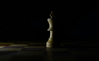 Wooden king chess piece standing alone on a dimly lit chessboard, symbolising strategy, leadership and decision-making in business.