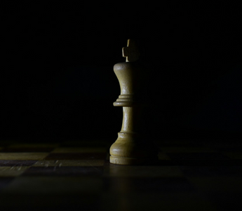 Wooden king chess piece standing alone on a dimly lit chessboard, symbolising strategy, leadership and decision-making in business.