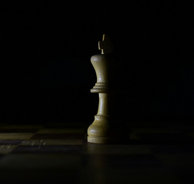 Wooden king chess piece standing alone on a dimly lit chessboard, symbolising strategy, leadership and decision-making in business.