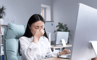 A stressed office employee showing signs of illness while working at her desk, highlighting rising workplace sick days and mental health-related absences in the UK.