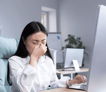 A stressed office employee showing signs of illness while working at her desk, highlighting rising workplace sick days and mental health-related absences in the UK.