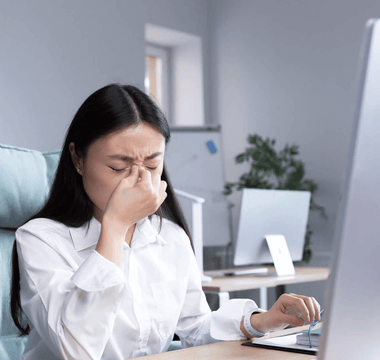 A stressed office employee showing signs of illness while working at her desk, highlighting rising workplace sick days and mental health-related absences in the UK.