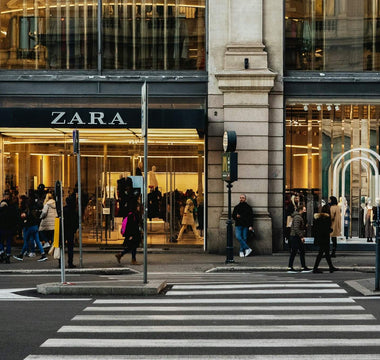 Shoppers outside a Zara store with large display windows and a pedestrian crossing in the foreground.