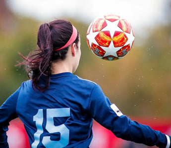 Female footballer in a blue shirt heading a football during a match.