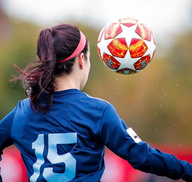 Female footballer in a blue shirt heading a football during a match.
