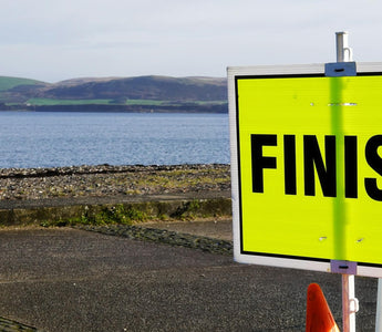 Bright yellow Parkrun finish sign by a coastal path, with sea and hills in the background, highlighting the inclusive community running event setting.