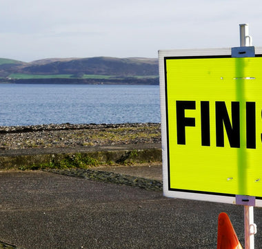 Bright yellow Parkrun finish sign by a coastal path, with sea and hills in the background, highlighting the inclusive community running event setting.