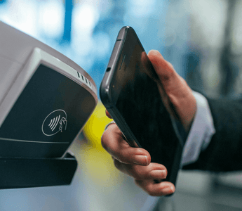 Hand holding a smartphone over a contactless payment terminal, illustrating the shift from cash to digital payments.