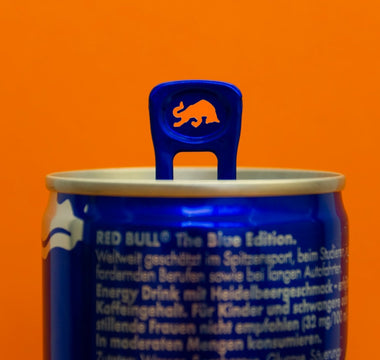Close-up of a Red Bull Blue Edition can with a raised blue pull tab featuring a bull-shaped cut-out, against an orange background.