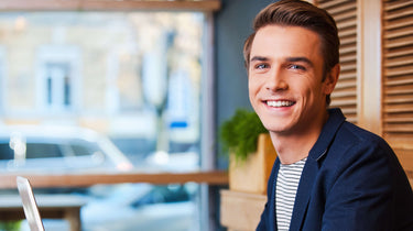Man sitting in a cafe smiling with a blurred outdoor background
