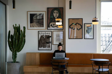 Person using a laptop at a table in a modern cafe with wall art and a cactus plant.