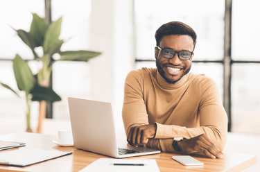 Man sitting at a desk studying for his CMA course with a laptop, smiling in an office setting